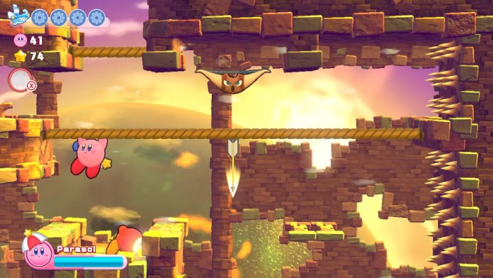 Kirby grimpe sur une corde et s'éloigne d'un arc et d'une flèche ennemie dans un niveau de Kirby's Return to Dream Land Deluxe pour Nintendo Switch.